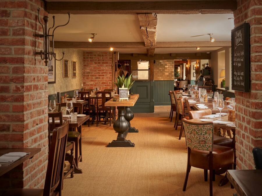 A restaurant with brick walls, wooden tables, and chairs. There are menus on the walls and a chalkboard menu on the right.