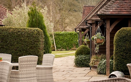 A patio area with wicker chairs, a wooden pergola, and neatly trimmed hedges.
