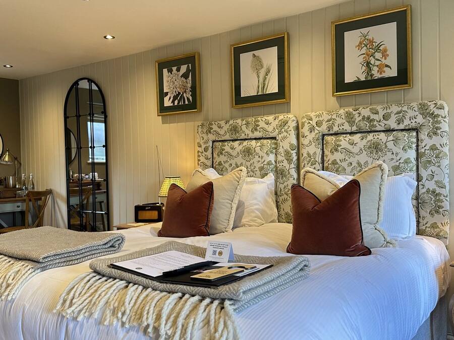 A hotel room with a large bed, a wooden nightstand, a mirror, and framed floral artwork on the walls.