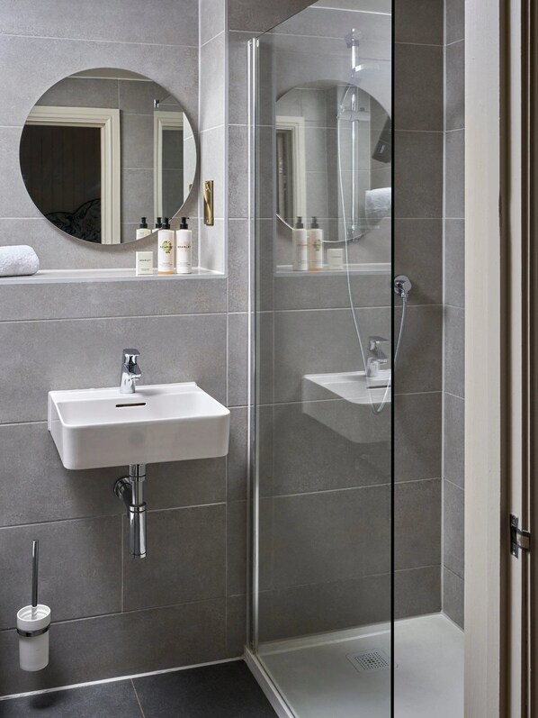 A modern bathroom with a glass-enclosed shower, a round mirror, and a white sink. - The White Horse (Chichester)