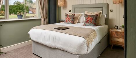 A neatly made bed with a book, a bedside table with a clock, and a window with curtains.