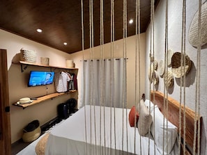 Une chambre d’hôtel avec un lit, un téléviseur posé sur une étagère et une tête de lit en bois.