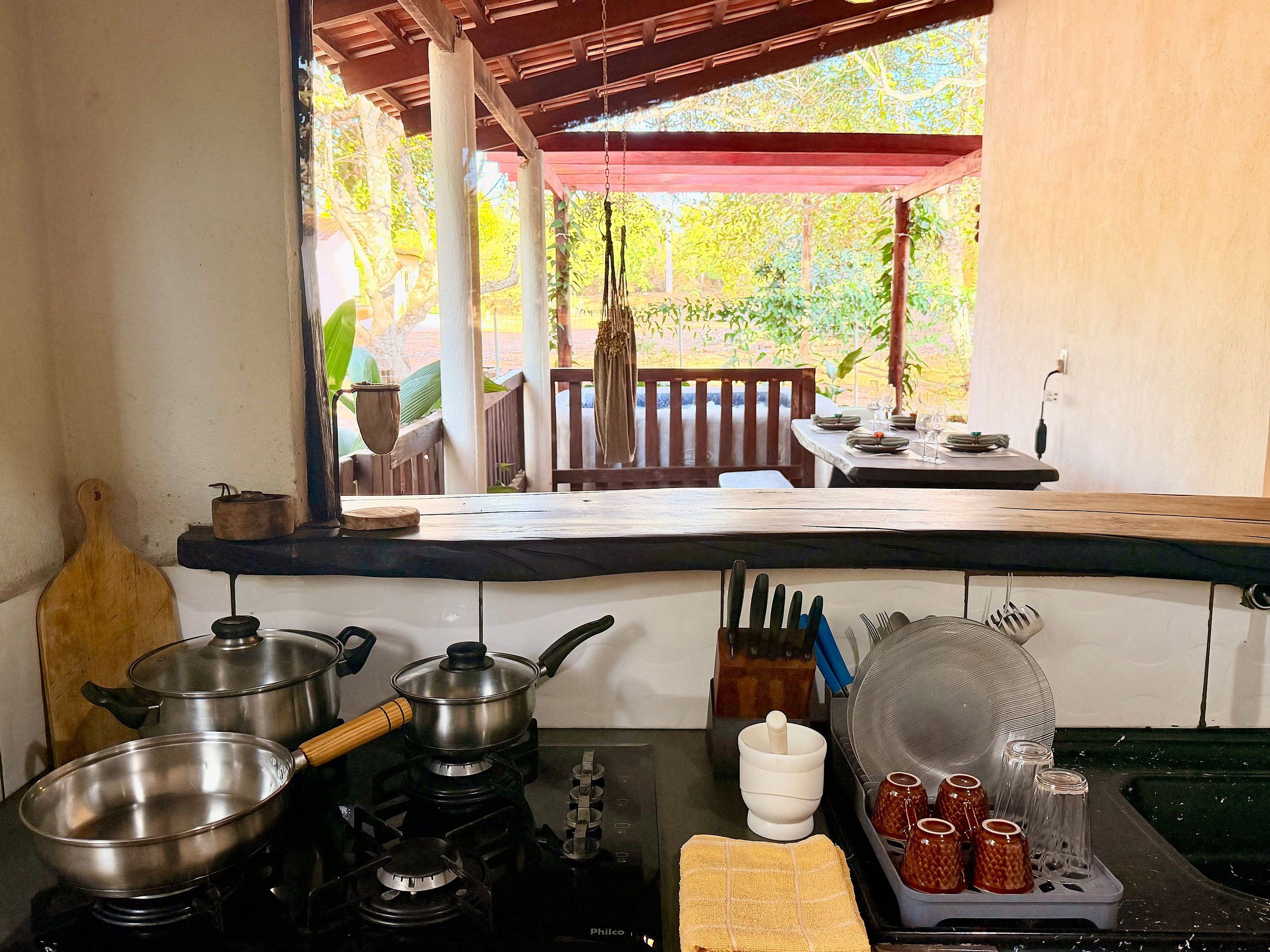 Una cocina con estufa a gas, ollas, tabla de cortar y ventana con vistas a un jardín.