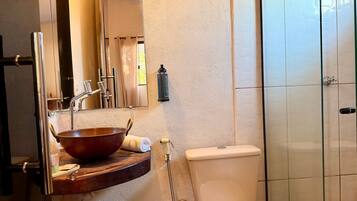 Un baño con tocador de madera, un espejo grande, un lavabo con cuenca de cobre, un inodoro y una zona de ducha.