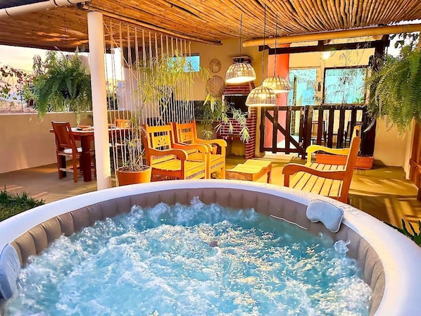 Un espace extérieur aménagé avec un jacuzzi, des chaises et des tables en bois, entouré de plantes en pot et doté d’un plafond en bambou.