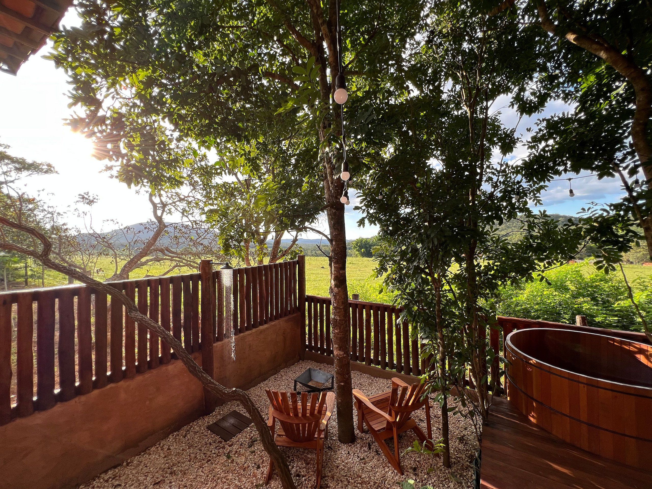 Un espacio al aire libre con sillas y una mesa de madera, rodeado por una valla y árboles.