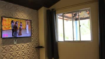 A room with a television mounted on a textured wall, a window with curtains, and a ceiling with wooden beams.