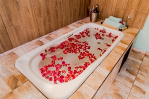 A bathtub filled with rose petals, a metal bucket with a bottle, and a towel on the side. - Shambala Piri (Pirenópolis)