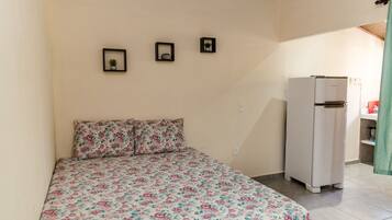 A bedroom with a bed, a white refrigerator, and three framed pictures on the wall.