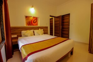 A bedroom with a large bed, wooden headboard, and a painting above it. There are two wooden doors and a light fixture on the wall. - OYO 9792 Home 2BHK Poolside Siolim (Oxel)
