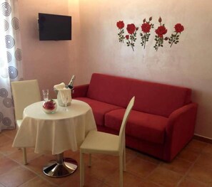 Un comedor con una mesa redonda, sillas, un sofá rojo y un televisor montado en la pared.