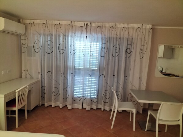 A room with a desk, two chairs, a window with blinds, and a mirror on the wall. - B&B Il Quadrifoglio di Tropea (Tropea)
