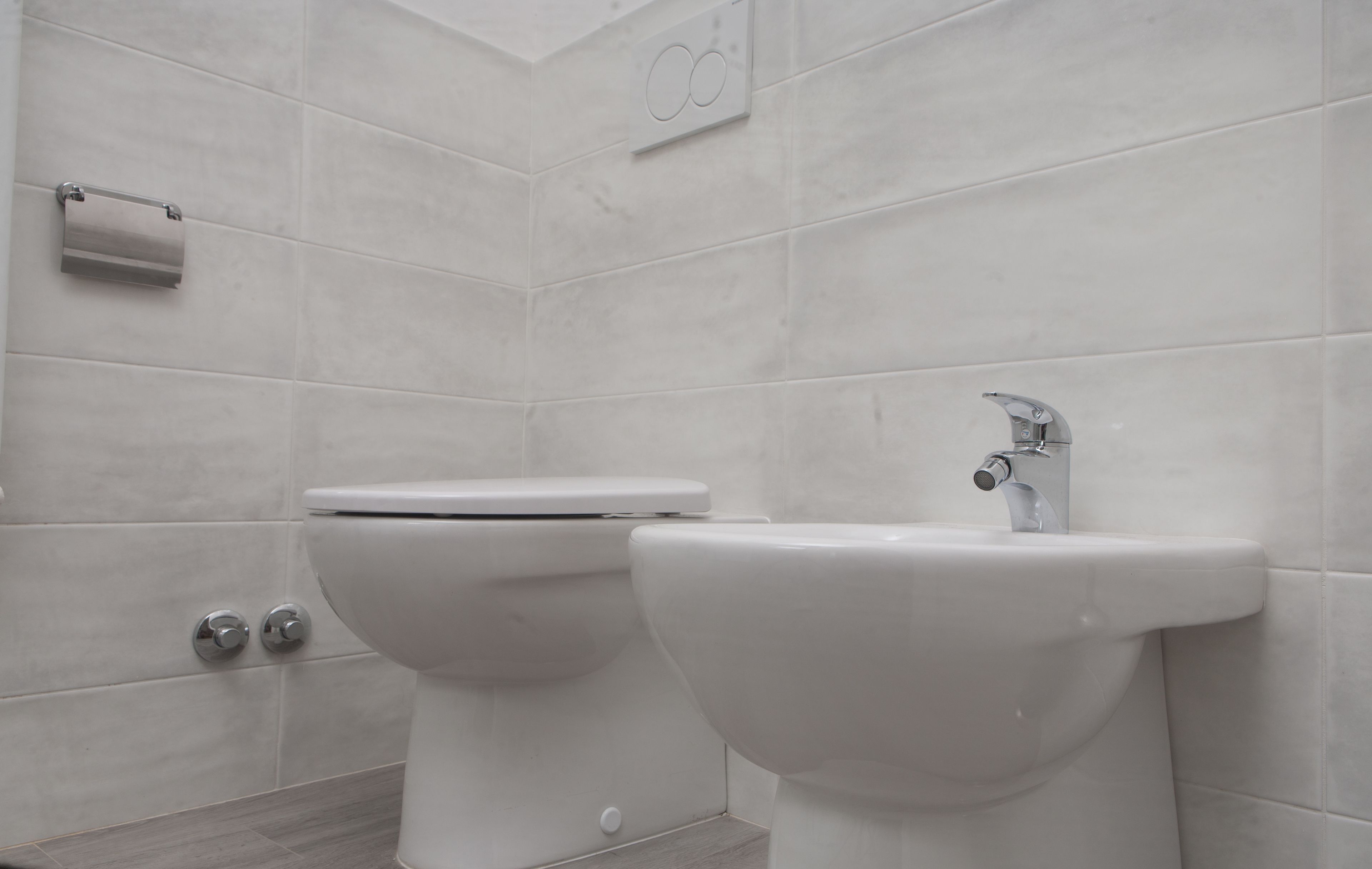 A modern bathroom with a toilet and bidet, tiled walls, and a toilet paper holder.