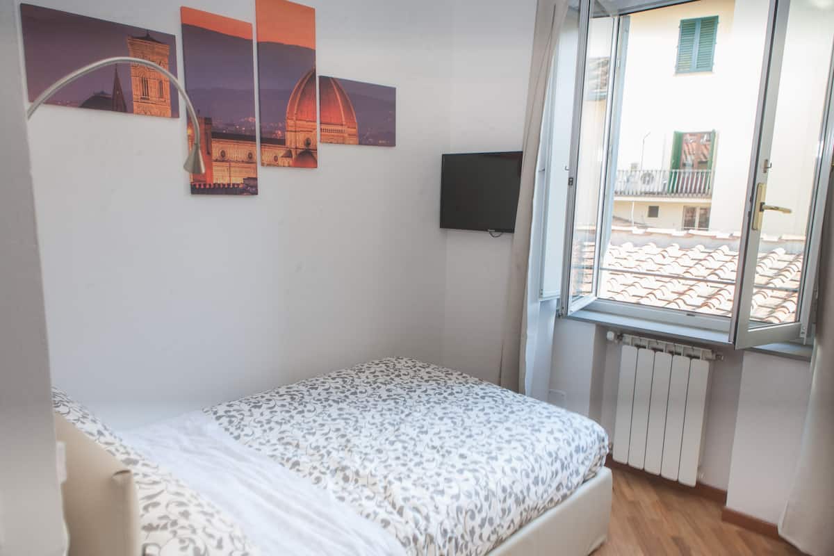 Ein Schlafzimmer mit einem Bett, einem Fenster mit Blick auf Gebäude und drei an der Wand befestigten Bildern.