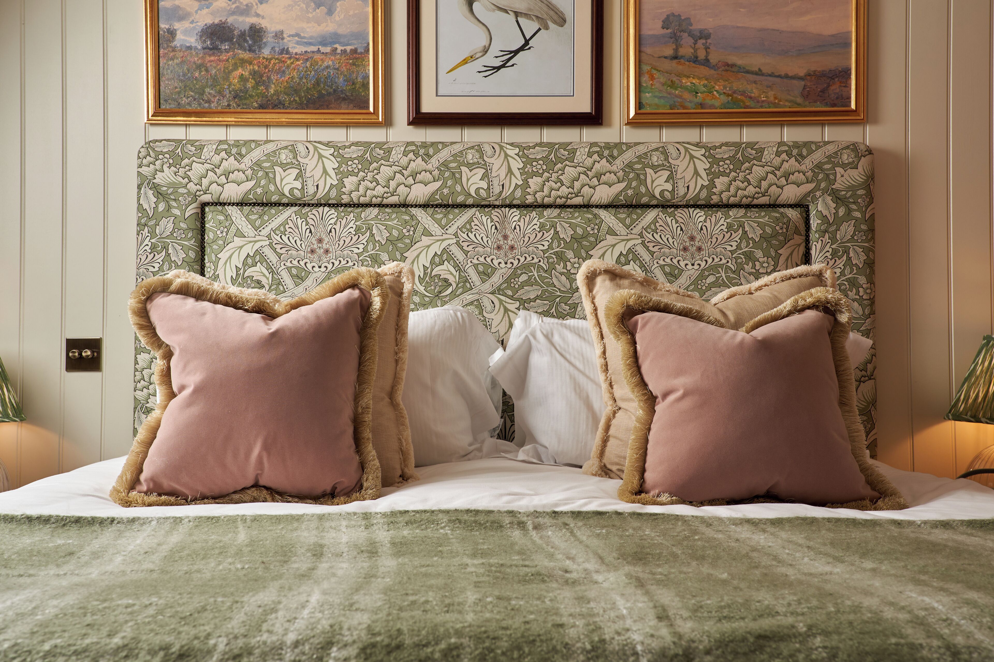 Un lit avec une tête de lit à motifs, deux oreillers roses et une couverture verte.