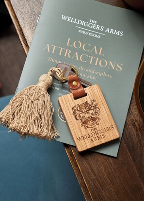 A book titled "The Welldiggers Arms Pub & Rooms" with a wooden bookmark featuring a coat of arms. - The Welldiggers Arms (Petworth)