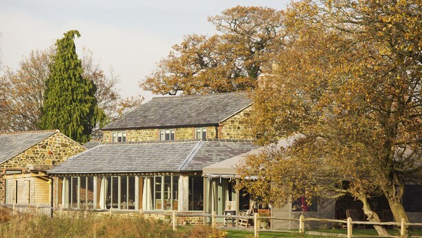 A stone building with a glass conservatory, surrounded by trees and a wooden fence. - The Welldiggers Arms (Petworth)