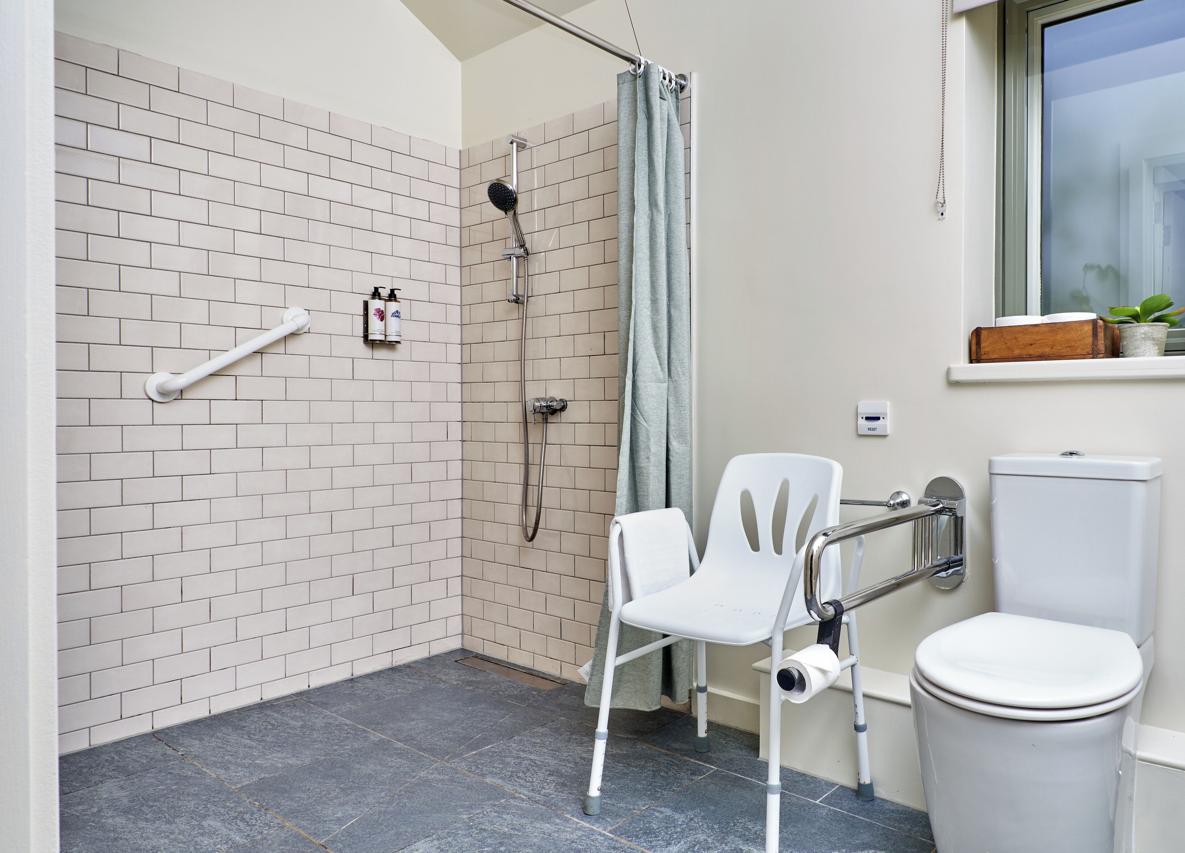A bathroom with a shower, toilet, and a white chair.
