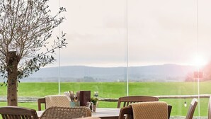 A dining area with a table and chairs, a small table with a plant, and a view of a green field and mountains. - The Welldiggers Arms (Petworth)
