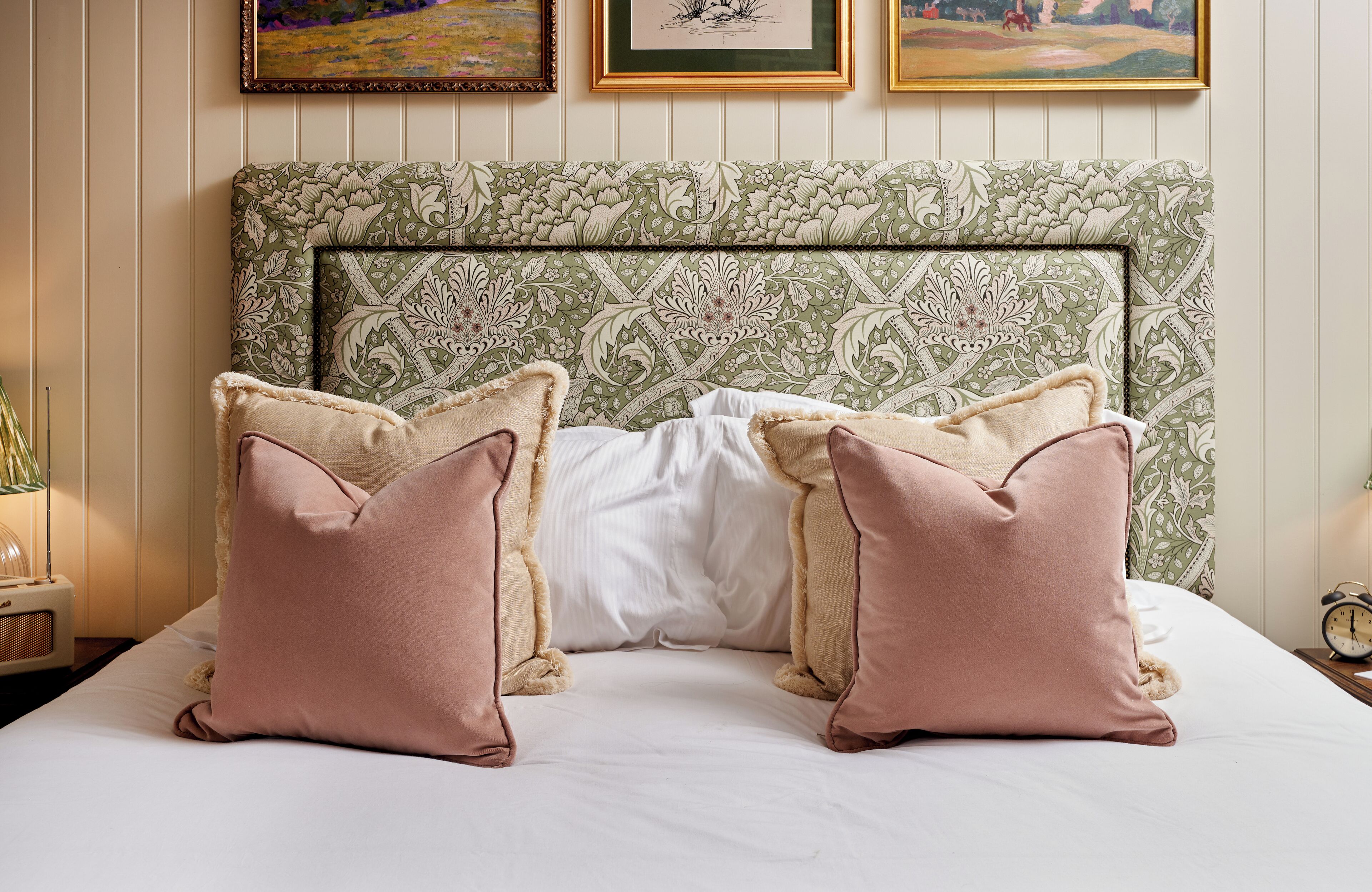 A neatly made bed with two pink pillows and a green patterned headboard.