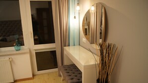 Ein modernes Schlafzimmer mit Glastisch, rundem Spiegel, gepolstertem Sitzbank und einem Fenster mit Vorhängen.