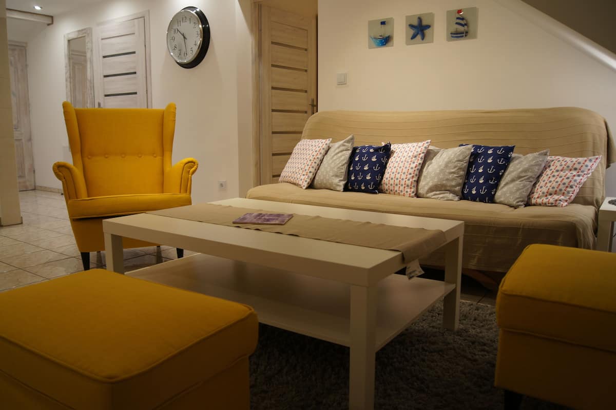 Un salón con un sillón amarillo, un sofá beige con cojines estampados, una mesa de centro blanca y una mesita auxiliar.