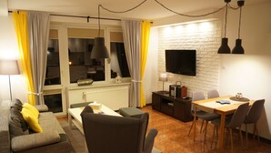 Ein modernes Wohnzimmer mit Sofa, Esstisch, Stühlen und einem Fernseher an einer Ziegelwand.