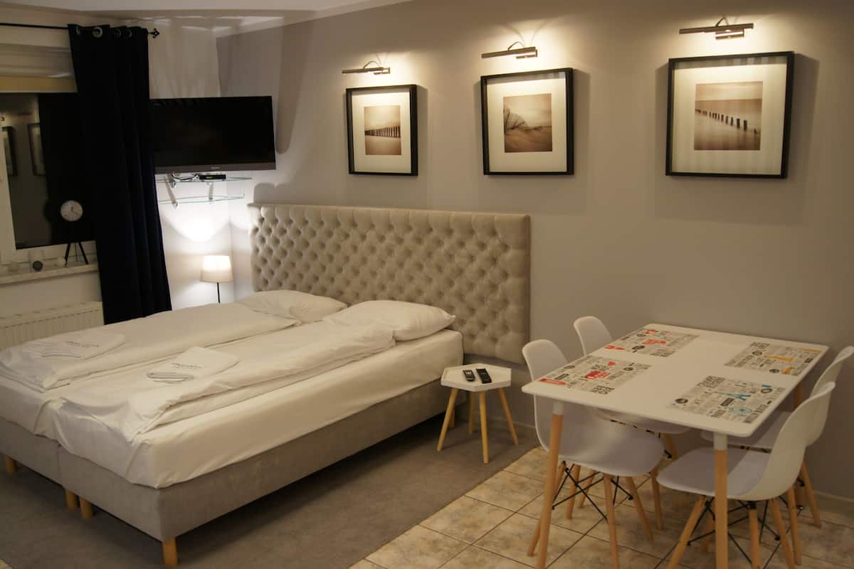 Habitación de hotel con cama, una pequeña mesa con sillas, televisor y cuadros en la pared.