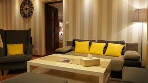 Ein Wohnzimmer mit Streifenmuster an der Wand, einer Uhr und einem Sofa mit gelben Kissen.