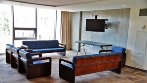 Un espace de détente moderne avec des canapés et une table, de grandes fenêtres et un téléviseur fixé au mur.
