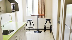 Une cuisine équipée d’un évier, d’un four à micro-ondes, de deux tabourets et d’une fenêtre avec des rideaux.