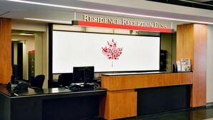 Un comptoir d’accueil doté d’un grand écran affichant le logo d’un érable rouge, d’un comptoir en bois et de chaises de bureau noires.