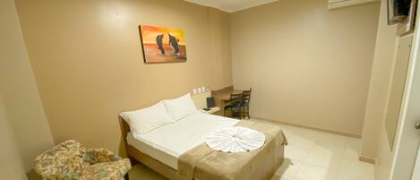 A hotel room with a bed, a chair, a desk, and a painting on the wall.
