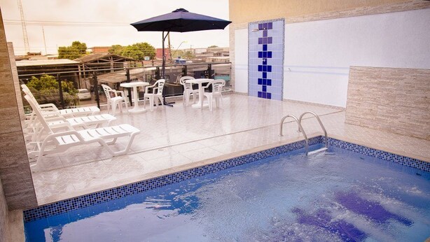 A rooftop pool area with lounge chairs and a table, surrounded by a tiled pool with a blue border. - Hotel Caribe (Porto Velho)