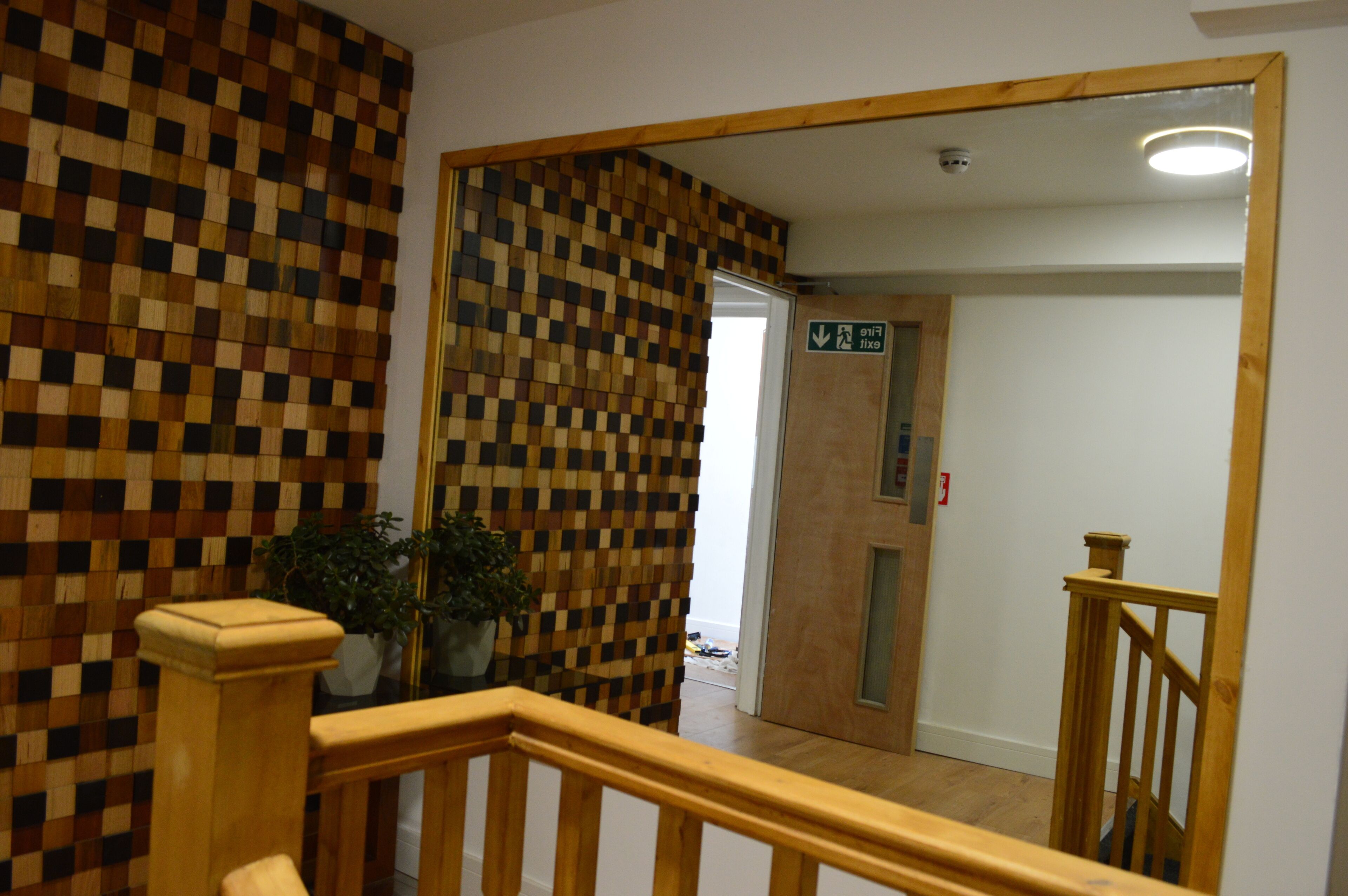 A hallway with a checkered wall pattern, wooden railings, and potted plants.