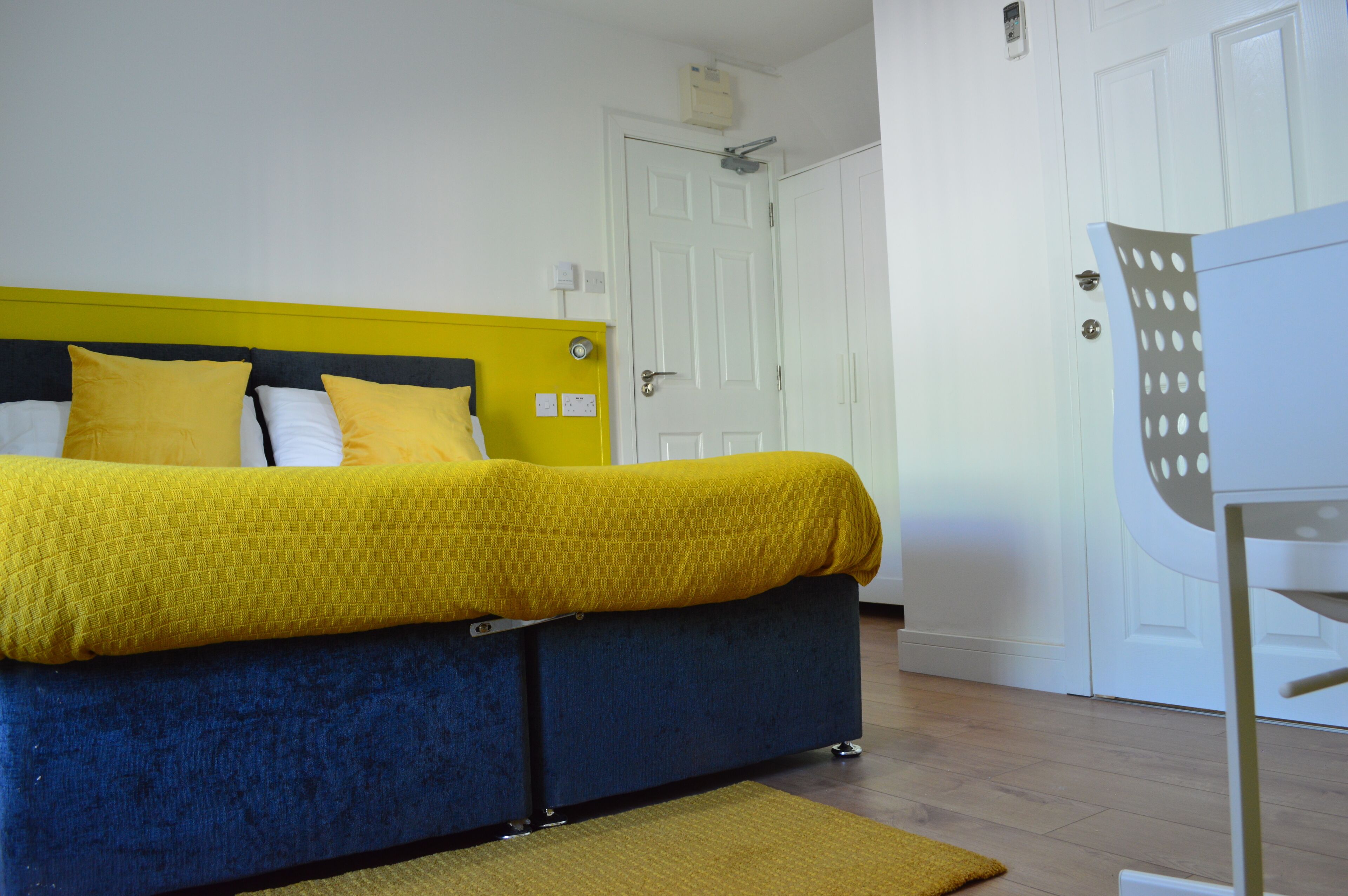 A bed with a yellow and blue headboard, a white door, and a white wardrobe with a polka dot design.