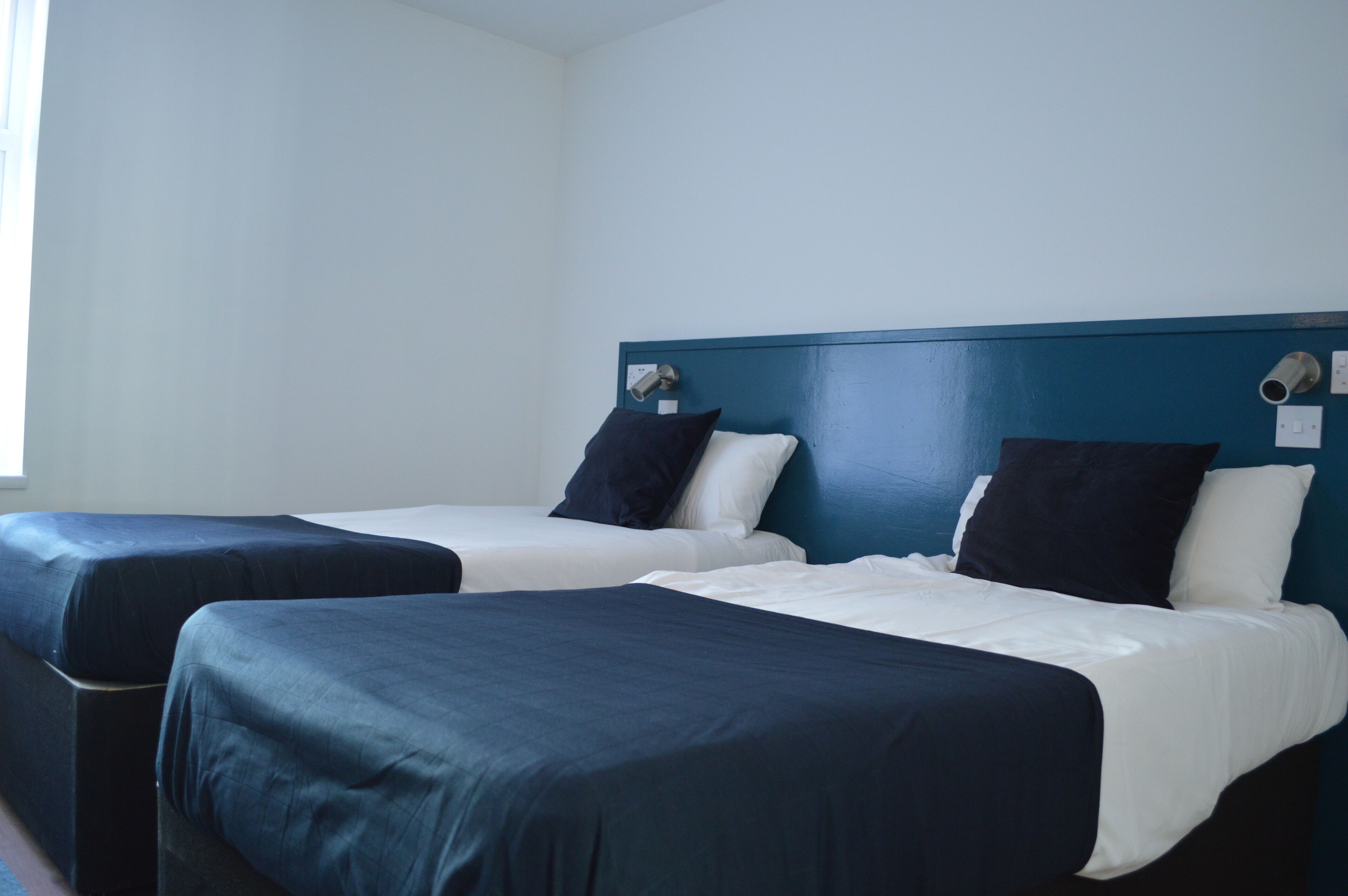 A hotel room with two beds, each with a blue and white bedspread, and a blue headboard.
