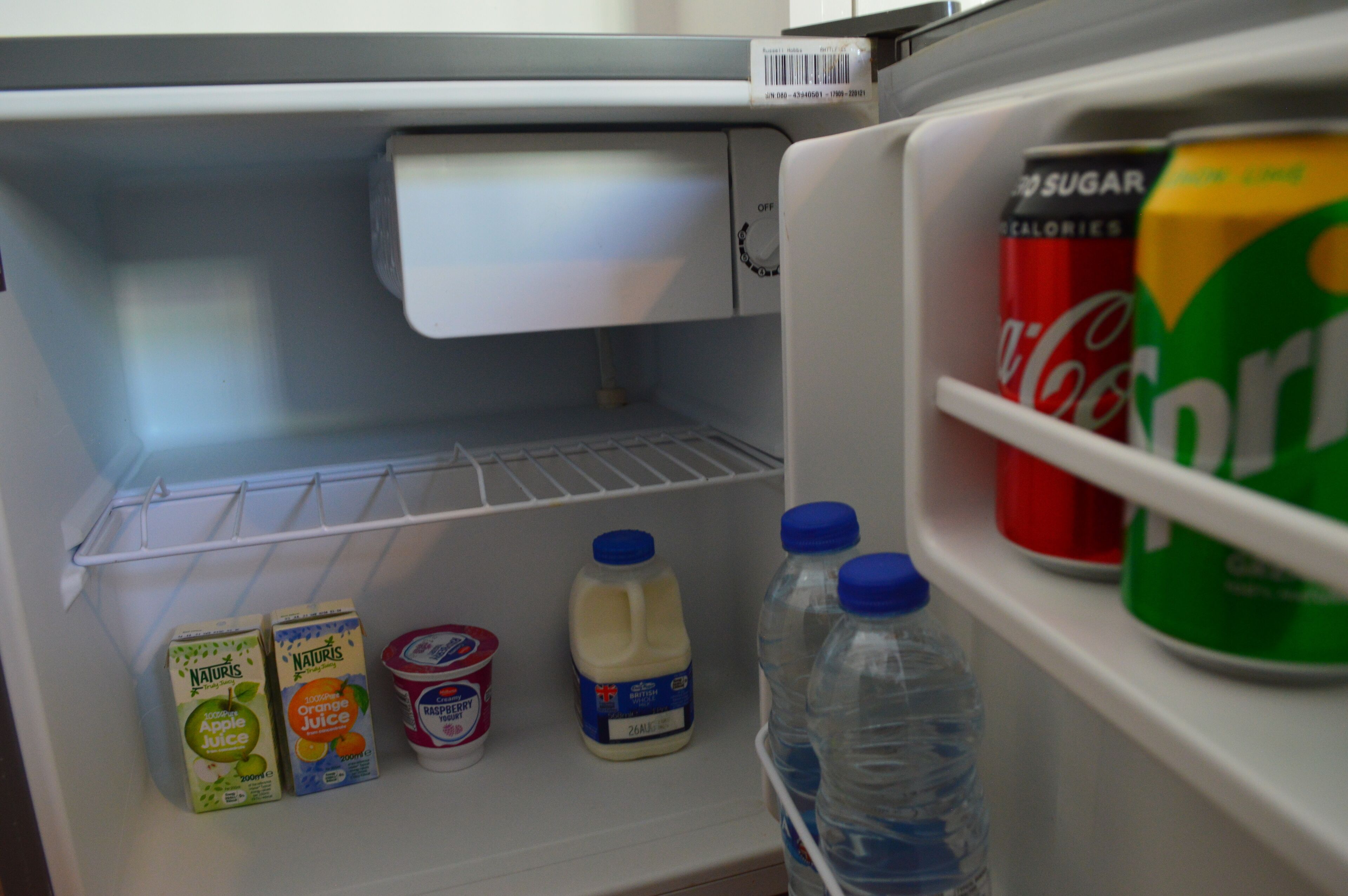 Frigorifero aperto con ripiani contenenti diverse bevande, tra cui succo di mela, succo d'arancia e latte.