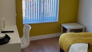 A bedroom with a bed, a desk, a chair, a TV, and a window with blinds.