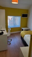 Un dormitorio con cama, escritorio, silla, televisión y ventana con persianas.