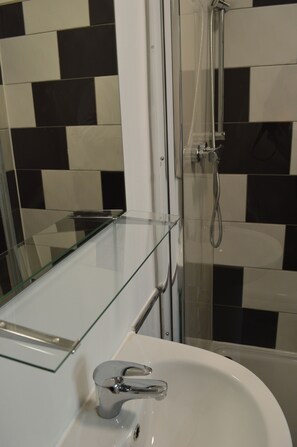 A bathroom with a glass shelf, a sink, and a shower area. - The Bell Gate House (Leicester)