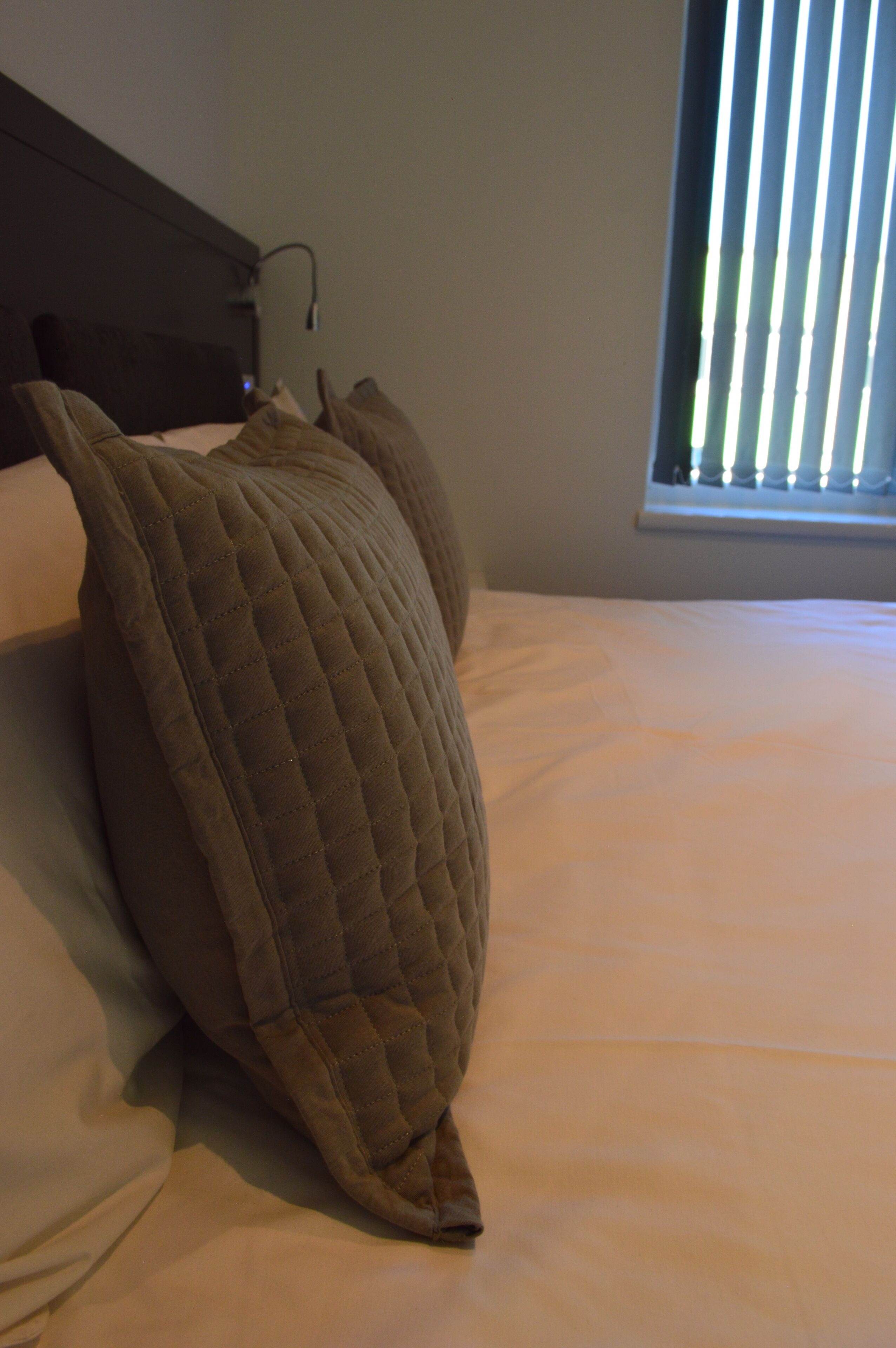 A bed with a quilted pillow and a plain white mattress.