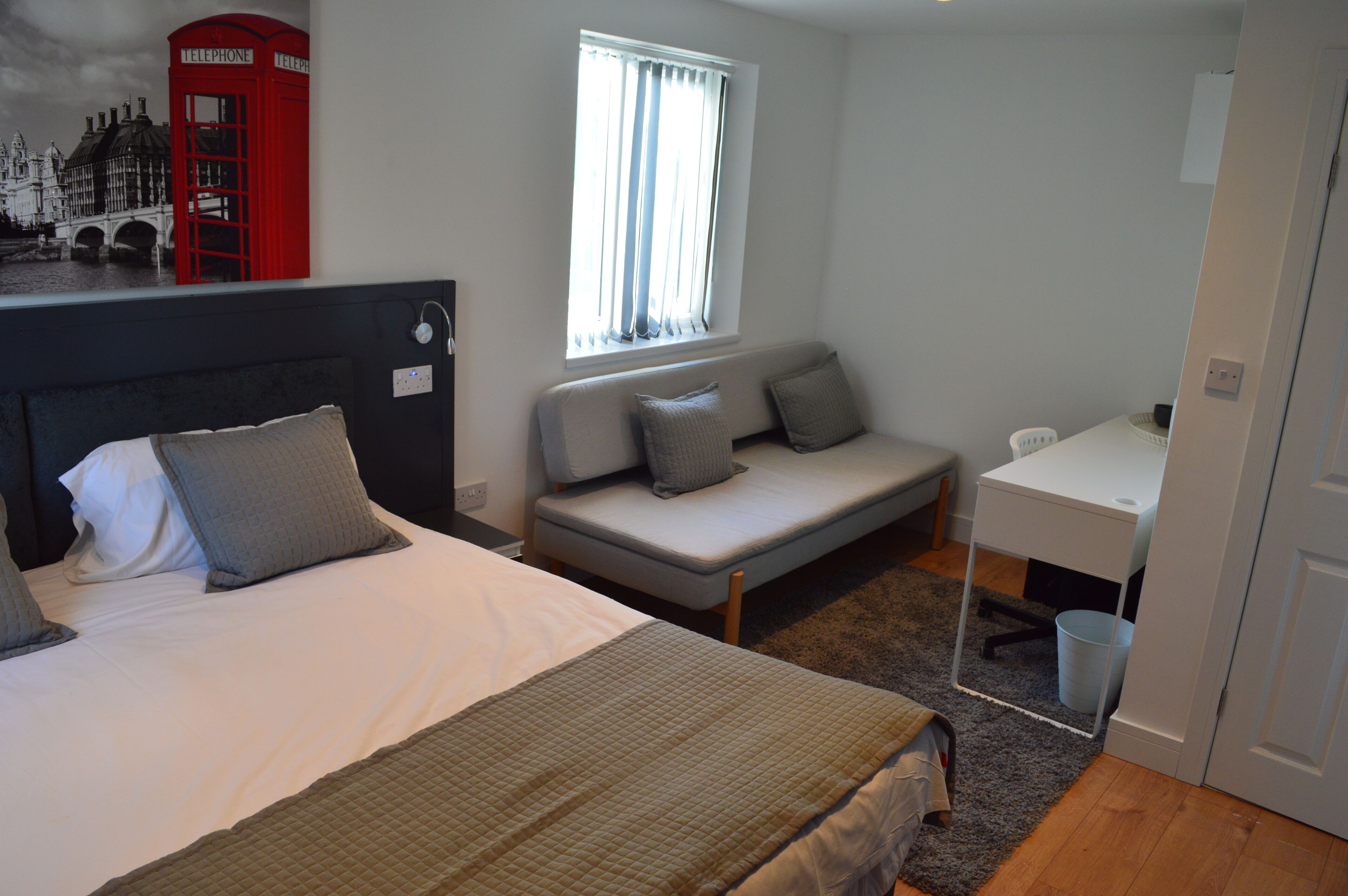 A bedroom with a bed, a sofa bed, a desk, and a window with curtains.