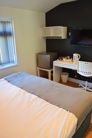 A hotel room with a bed, a desk, a television, and a window with curtains. - The Bell Gate House (Leicester)