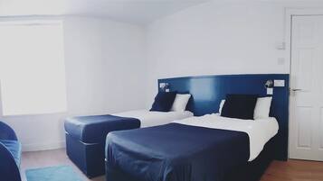 A room with two beds, a window, a door, and a blue chair.