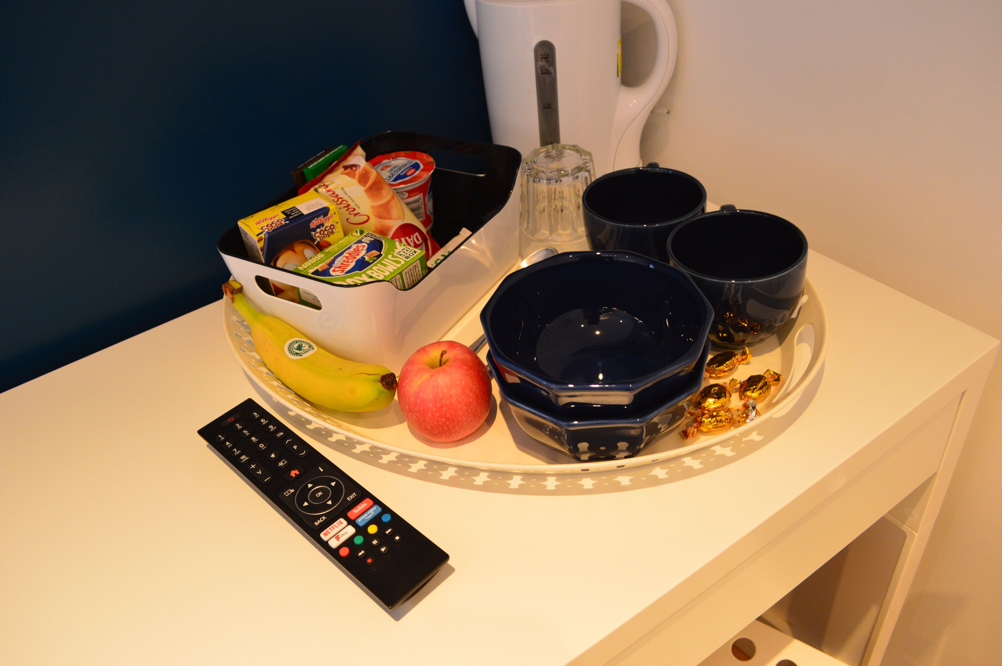 A tray with snacks, a banana, an apple, and a remote control on a table.