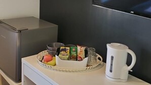 A compact kitchenette with a refrigerator, a microwave, a small sink, and a white countertop. There is a TV mounted on the wall and a basket with food items on the countertop. - The Bell Gate House (Leicester)