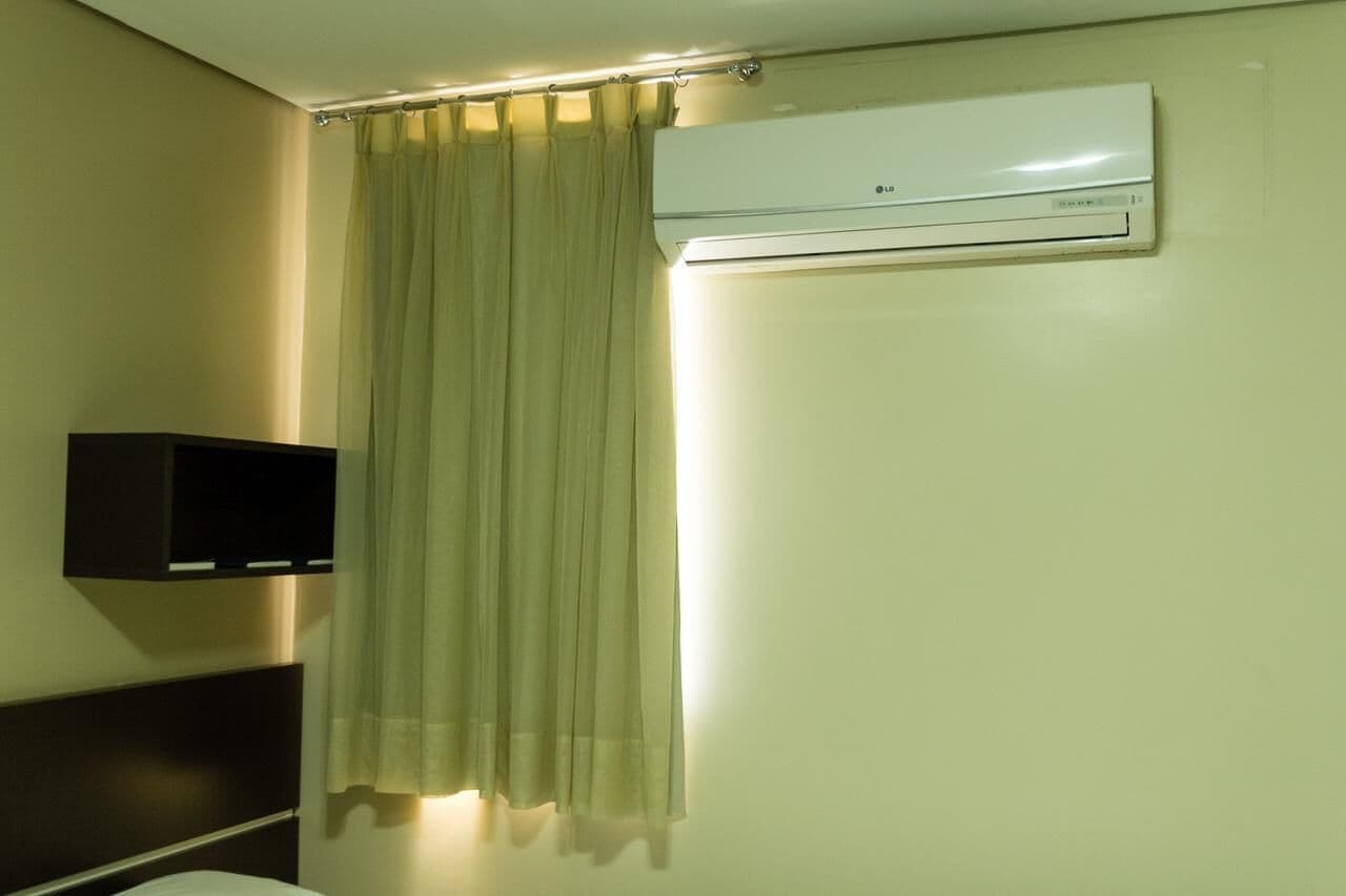 Quarto de hotel com cama, mesa de cabeceira, ar condicionado fixado na parede e cortina.