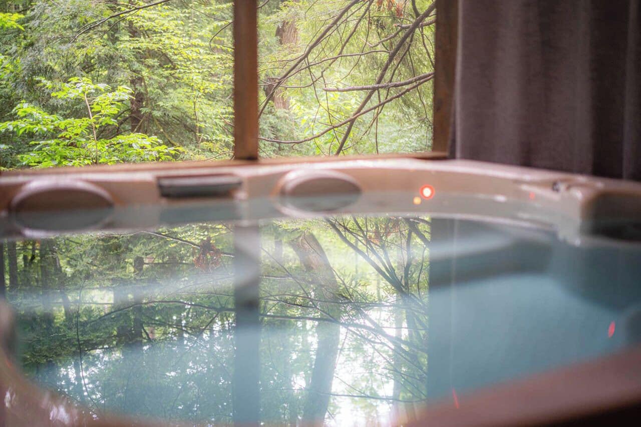 A hot tub with a view of a forest through a window.