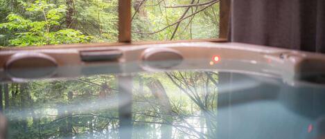 A hot tub with a view of a forest through a window.